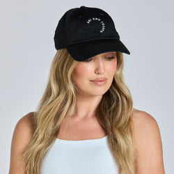 Woman wearing a black cap and white sports bra against a gray background